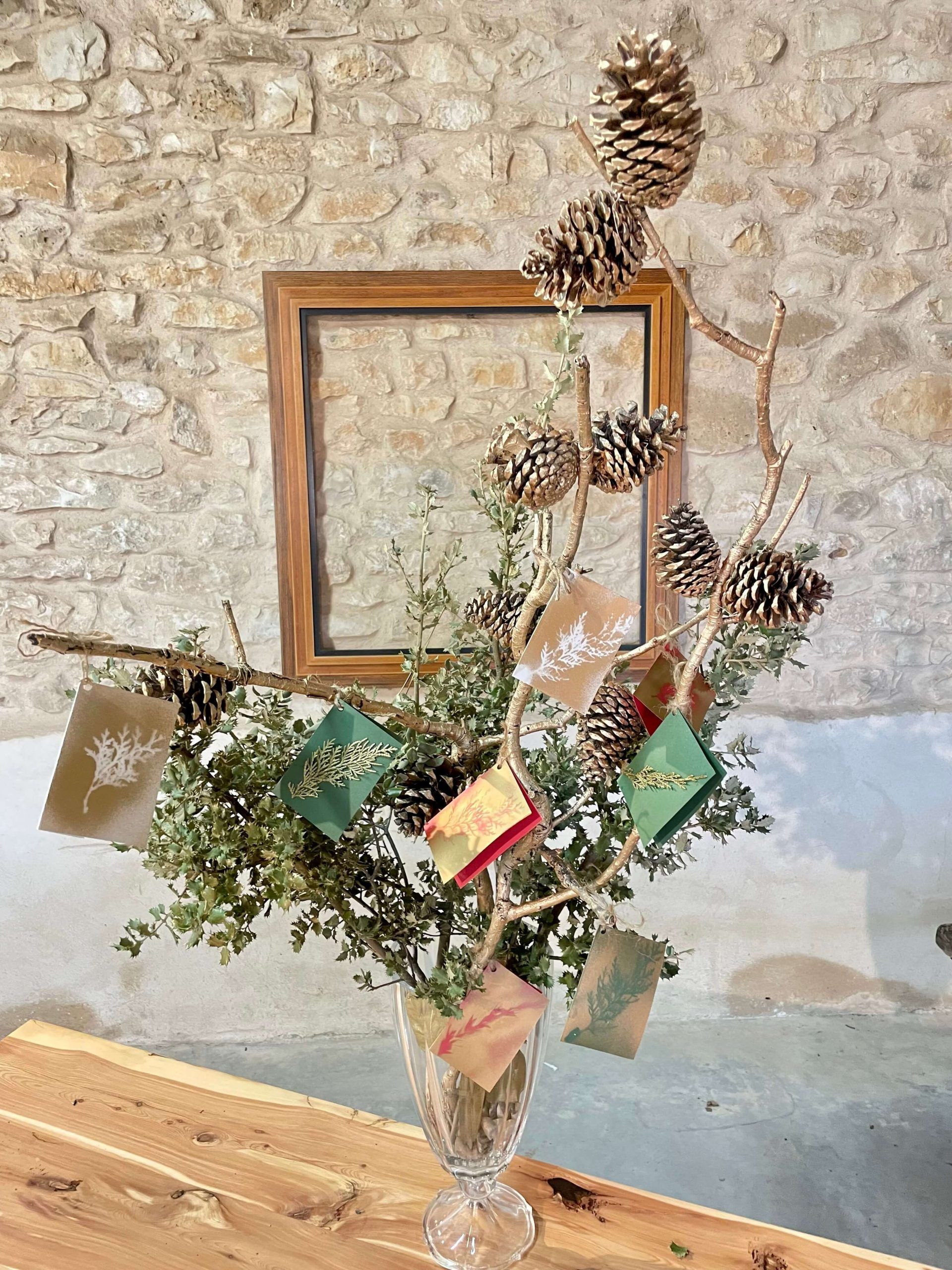 Centro decorativo navideño en copa con piñas y tarjetas