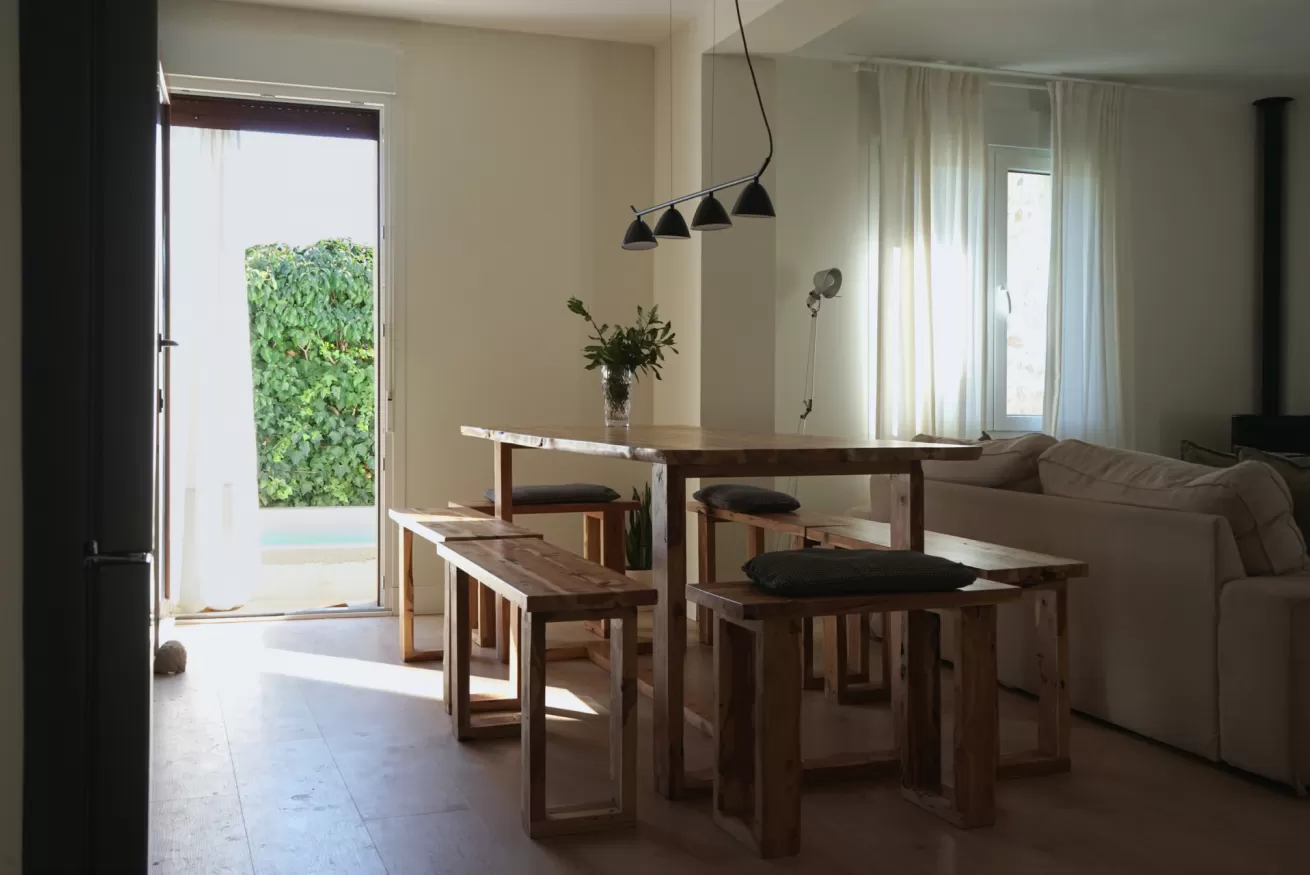 Zona de comedor interior de La Casa del Palomar con mesa de madera y vistas al jardín privado, casa rural en Vadocondes, Burgos